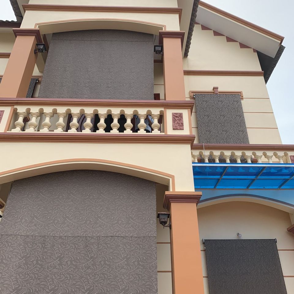 Rèm lưới cuốn phủ trước ban công kính, cây trồng ở hai bên.