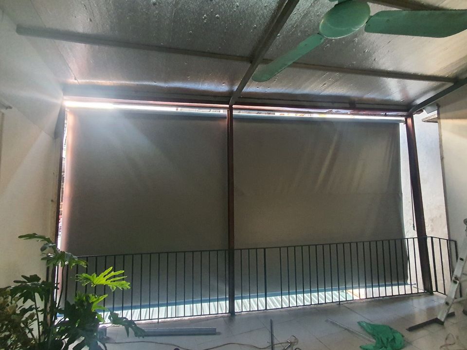 Mành màu xám hạ trước ban công có lan can và cây xanh.
